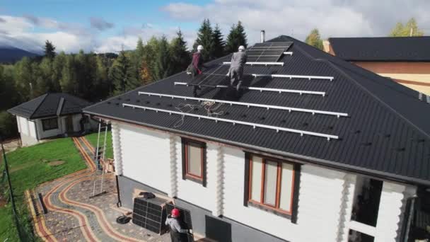 在房顶上建造太阳能电池板系统的技术人员的空中视图 戴钢盔的男工在室外携带光电太阳能组件 替代能源和可再生能源的概念 — 图库视频影像