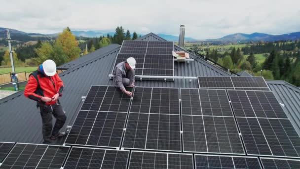 屋根の上に太陽光発電パネルを設置する技術者 六角キーの助けを借りて太陽電池モジュールシステムを構築ヘルメットの男性エンジニアのドローンビュー 代替的再生可能エネルギーの概念 — ストック動画