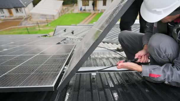 太陽光発電パネルの専門家接続ケーブル 家の上にPv太陽電池のインストール 屋根の上に太陽電池パネルのケーブルを確保白いヘルメットの労働者 — ストック動画