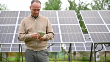 Gülümseyen adam güneş panellerine yatırım yaparak ne kadar kazandığını sayıyor. Erkek kazancından memnun. Alternatif enerji ve yatırım kavramı.