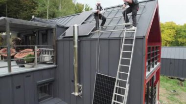 Erkek işçiler evin çatısına güneş paneli kuruyor. Kasklı elektrikçiler fotovoltaik güneş modülünü açık havada kaldırıyorlar. Alternatif ve yenilenebilir enerji kavramı.