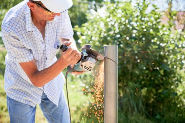 Metal direği öğütücüyle kesen erkek işçi. Güneş paneli kurulumu için alüminyum çubuk hazırlarken el bilgisayarı kullanan koruyucu gözlüklü bir adam..