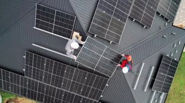 Teknisyenler evin çatısına güneş paneli inşa ediyorlar. Fotovoltaik güneş modülü taşıyan miğferli işçilerin insansız hava aracı görüntüsü. Alternatif ve yenilenebilir enerji kavramı.