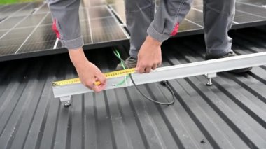Becerikli teknisyenlerin tam hesaplamalar için ölçümler yapmalarına yakından bakın. Çatıdaki PV güneş paneli ayarlanıyor. Miğferdeki mühendis bir mezura ile güneş hücresinin hesaplamalarını yapıyor..