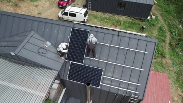 屋根の上に太陽電池モジュールステーションを構築する技術者 太陽電池パネルシステムを屋外に設置ヘルメットの男性電気技師 代替エネルギーと再生可能エネルギーの概念 空中風景 — ストック動画