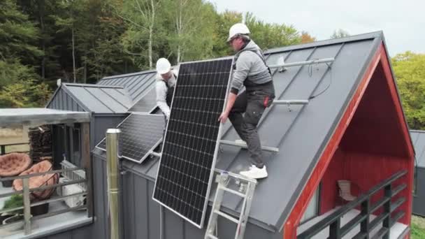 技术人员在房顶上安装太阳能电池板系统 戴钢盔的男工在室外携带光电太阳能组件的空中照片 替代能源和可再生能源的概念 — 图库视频影像