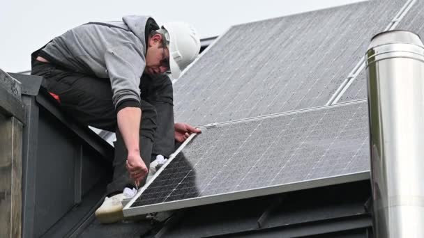 人工技术人员在房顶上安装光电太阳能电池板 头盔工程师安装太阳能模块系统 在雨中使用六角键 可再生能源的替代概念 — 图库视频影像