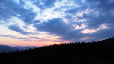 Renkli, dramatik bulutlu gökyüzü altında ağaçlarla çevrili dağ ormanlarının video görüntüleri. Dağlarda, çam ağaçları ve çimenli tepelerle gün batımının resimli manzarası. Doğanın güzelliği konsepti.