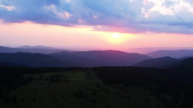 Dağlardaki çimenli tepelerin üzerinde güzel, dramatik bulutlu gökyüzünün video görüntüleri. Renkli akşam gökyüzü altında bulutlu ve batan güneşli dağ tepelerinin resimli manzarası. Doğanın güzelliği konsepti.