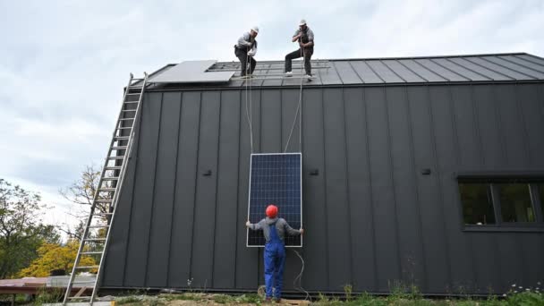 在房顶安装太阳能电池板系统的男工 戴钢盔的电工在室外用绳索提起光伏太阳能组件 替代能源和可再生能源的概念 — 图库视频影像