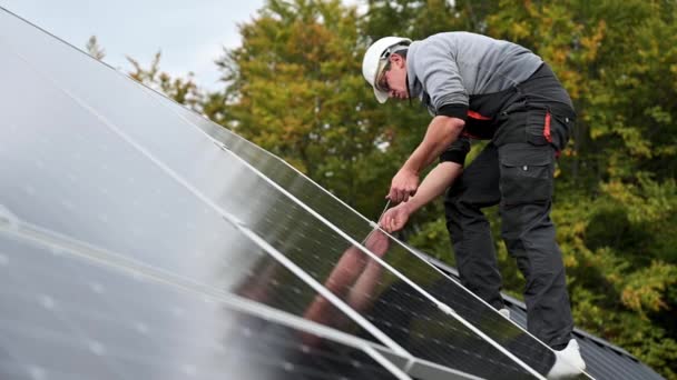 家の屋根の上に太陽光発電パネルをマウントする人技術者 六角キーの助けを借りて太陽電池モジュールシステムをインストールヘルメットのエンジニア 代替的再生可能エネルギーの概念 — ストック動画