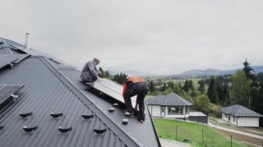 Teknisyenler evin çatısına fotovoltaik güneş modülü istasyonu inşa ediyorlar. Miğferli elektrikçiler güneş paneli sistemi kuruyor. Alternatif ve yenilenebilir enerji kavramı. Hava görünümü.