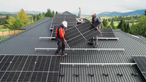 技术人员在房顶上建造太阳能电池板系统 关于戴钢盔的男工在室外携带光伏太阳能组件的无人驾驶图片 替代能源和可再生能源的概念 — 图库视频影像
