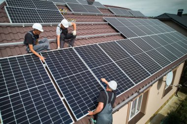 Erkek teknisyenler fotovoltaik güneş modüllerini evin çatısına monte ediyorlar. Kasklı işçiler dışarıda güneş paneli sistemi kuruyor. Alternatif ve yenilenebilir enerji kavramı. Hava görünümü.