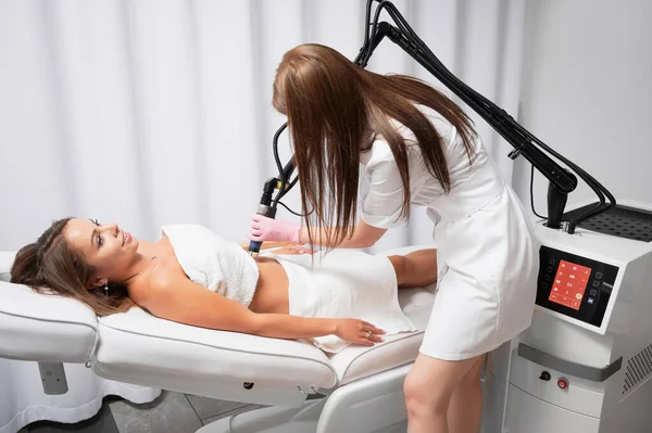 Beautician performing laser resurfacing of abdomen, ridding patient of stretched skin. Fractional CO2 laser is modern device for treatment of skin defects, scars and stretch marks after childbirth.