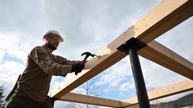 Man worker building wooden frame house on pile foundation. Carpenter hammering bolt into wooden plank, using hammer. Carpentry concept.