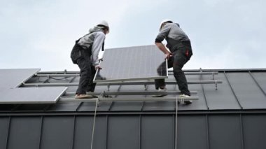 Teknisyenler evin çatısına güneş paneli kuruyor. Dışarıda fotovoltaik güneş modülü taşıyan miğferli işçiler. Alternatif ve yenilenebilir enerji kavramı.
