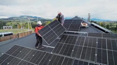 Teknisyenler evin çatısına güneş paneli inşa ediyorlar. Fotovoltaik güneş modülü taşıyan miğferli işçilerin insansız hava aracı görüntüsü. Alternatif ve yenilenebilir enerji kavramı.