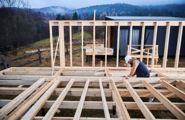 Yığınla temele ahşap çerçeve inşa eden bir işçi. Marangoz, çekiç kullanarak tahta kirişe çivi çakıyor. Marangozluk kavramı.