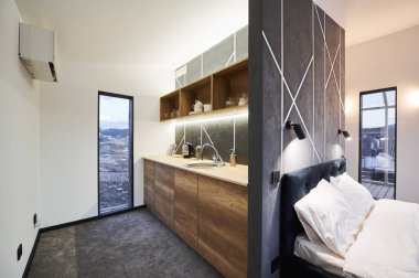Tam teçhizatlı mutfağın modern tasarımı ve dağ evindeki rahat yatak odası. Gri dekoratif duvarlar ve cam kapılarla ayrılmış açık alan manzaralı terasa çıkıyor. İç mekan kavramı.