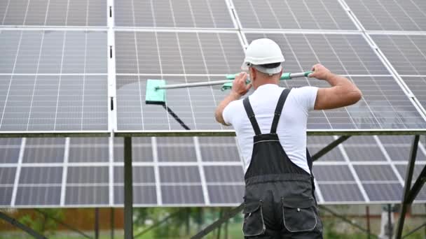 男人用拖把清洁太阳能光伏面板 对穿着工作服和头盔的工人照顾光电电池的背景图 替代能源创新概念 — 图库视频影像