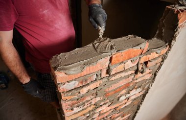 İnşaat halindeki binada tuğla döşeyen iş eldivenleriyle erkeklerin ellerini kapatın. Tuğlalara beton harç uygulayan tuğla ustası. Masonluk inşaat konsepti.