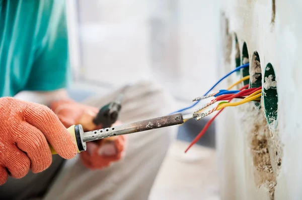 在正在翻新的公寓里安装电缆的同时 用电焊工具把戴工作手套的男人关起来 与电热器焊接铁打交道的男性电工 — 图库照片