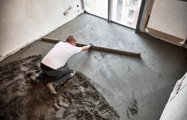 Erkek inşaat işçisinin zemine çimento karışımı bir şey döşediği en üst görüntü. Adam dairede zemini tararken düz kenarlı düzleştiriyor ve düzleştiriyor.