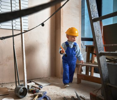 Tadilat altındaki dairede fırçası olan bir inşaat işçisi. Çocuk evde oynarken güvenlik kaskı takıyor ve tulum giyiyor..