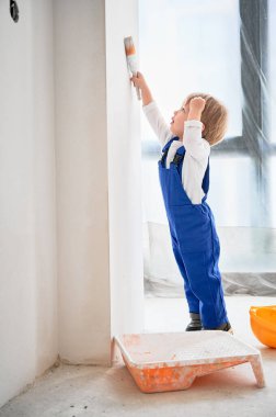 Duvarı boya fırçasıyla boyayan bir sürü çocuk inşaat işçisi. Çalışan bir çocuk evde tamirat sırasında boya fırçası kullanıyor..