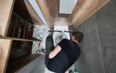 Bir adamın dairede tadilat altında sifonu çekerken ki görüntüsü. Erkek tesisatçı evde tuvalet tesisatı üzerinde çalışırken inşaat aletleriyle yere çömeliyor..
