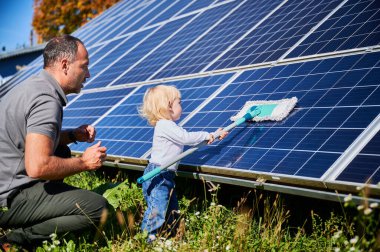 Father showing his little son the solar panels during sunny day. Cute boy helping his dad to clean solar battery. Young man teaching his small kid how to care about their source of energy.