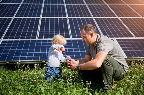 爸爸教他的小儿子如何在太阳能电池板的背景下使用螺丝刀 父亲教他的孩子如何使用工具 儿子和他的年轻爸爸学习工具 — 图库照片