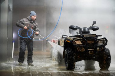 Full length of man cleaning quad bike with high pressure water sprayer at self-service car washing station clipart
