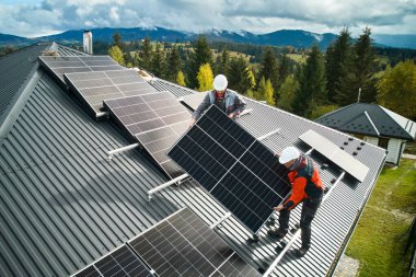 İşçiler evin çatısına güneş panelleri kuruyor. Dağlarda güneş pili kurulumu. Alternatif enerji kavramı.