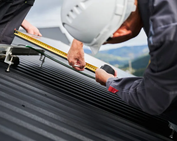 为精确计算而进行测量的合格技术人员的回顾 在屋顶上调整光伏太阳能电池板 利用测量带进行太阳能电池头盔计算的工程师 — 图库照片