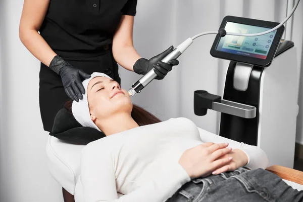 医生美容师在为病人进行面部整容手术时使用射频微调装置 躺在美容设备附近接受护肤治疗的妇女 — 图库照片