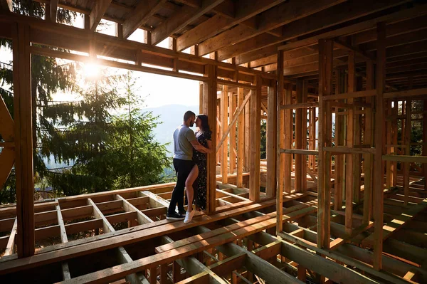 stock image Man and woman examining their future wooden frame dwelling nestled in the mountains near forest. Youthful couple at construction site in early morning. Concept of contemporary ecological construction.