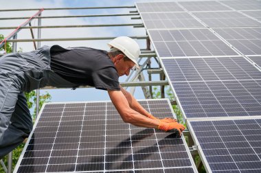 Cropped view of man engineer solar installer placing solar module on metal rails. Male worker installing photovoltaic solar panel system. Concept of alternative energy and power sustainable resources. clipart