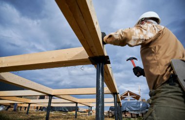Yığınla temele ahşap çerçeve inşa eden bir işçi. Marangoz çekiçle tahta tahtaya sürgüler, çekiç kullanır. Marangozluk kavramı.