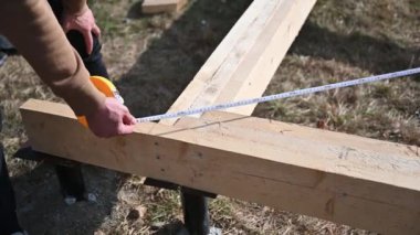 Man worker building wooden frame house on pile foundation. Close up carpenter using tape measure for measuring wooden planks. Carpentry concept.