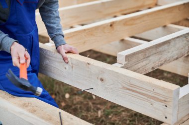 Yığınla temele ahşap çerçeve inşa eden bir işçi. Marangoz, çekiç kullanarak tahta kirişe çivi çakıyor. Marangozluk kavramı.