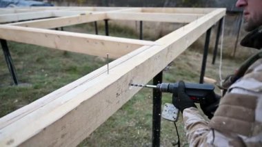 Man building wooden frame house. Worker drilling hole by electric drill in timber framing of future cottage. Carpentry concept.