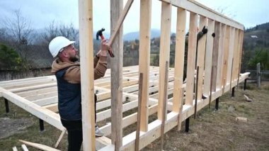 Yığınla temele ahşap çerçeve inşa eden bir işçi. Marangoz çekiçle tahta kirişe çivi çakıyor. Marangozluk kavramı.