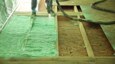 Erkek müteahhit ahşap iskeleti yalıtıyor. Adam işçi, gelecekteki kulübenin içine poliüretan köpük püskürtüyor, çoğul bileşen silah kullanıyor. İnşaat ve yalıtım konsepti.