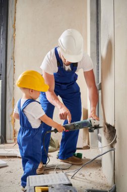 Elektirikli aletlerle çalışan bir adam ve küçük bir çocuk apartman dairesinde tadilat altında. İş tulumu ve güvenlik kaskı yapımcısı oğluna elektrikli öğütme makinesini nasıl kullanacağını öğretiyor..