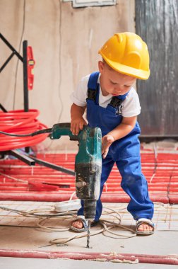 Güvenlik kasklı çocuk tadilat sırasında elektrikli çekiçle delme zemininde. Çocuk inşaat işçisi, daireye döşeme ısıtma sistemi kurarken sondaj makinesi kullanıyor..