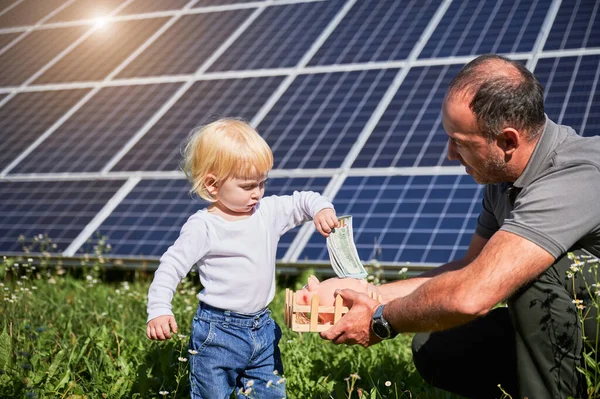 儿子和他爸爸存钱 存进储蓄罐 父亲教儿子将来如何在太阳能电池板上投资 节约资金 投资于可再生能源的概念 — 图库照片