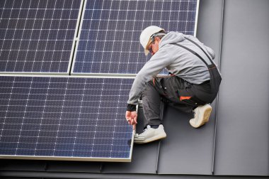 Evin çatısına fotovoltaik güneş panelleri monte eden teknisyen. Başlıktaki mühendis, uğursuz anahtarın yardımıyla güneş modülü sistemi kuruyor. Alternatif, yenilenebilir enerji kavramı.