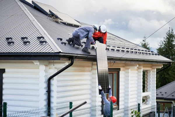 stock image Men mounters installing solar panel system on roof of house. Workers in helmets lifting up photovoltaic solar module outdoors. Concept of alternative and renewable energy.